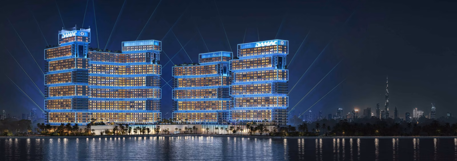 Chelsea Residences by DAMAC lit in Chelsea blue at night, with the Dubai skyline behind